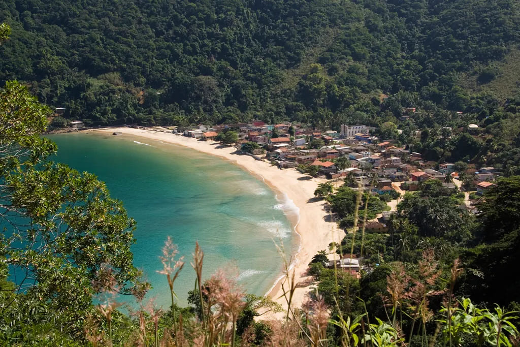 Vista aérea da Ilha Grande, Rio de Janeiro, com uma baía de águas azul-turquesa, areia clara e mata atlântica exuberante, um paraíso ecológico para casais."