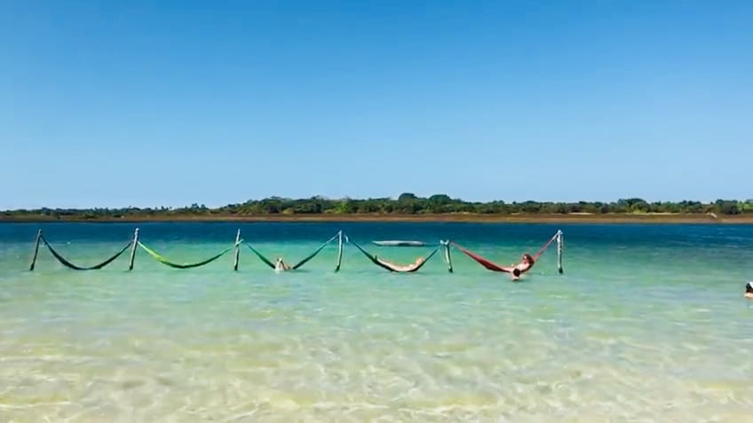 Pessoas relaxando em redes dentro da Lagoa do Paraíso em Jericoacoara, Ceará, com águas claras e céu azul, um cenário perfeito para casais.