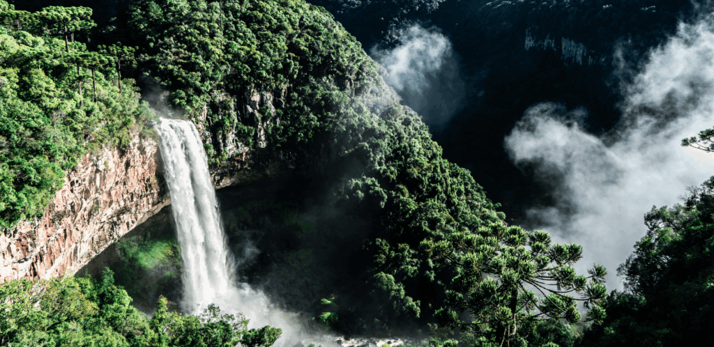 Vista da Cascata do Caracol em Canela, Rio Grande do Sul, com uma grande queda d'água cercada por vegetação densa e névoa, um destino de natureza e romance."