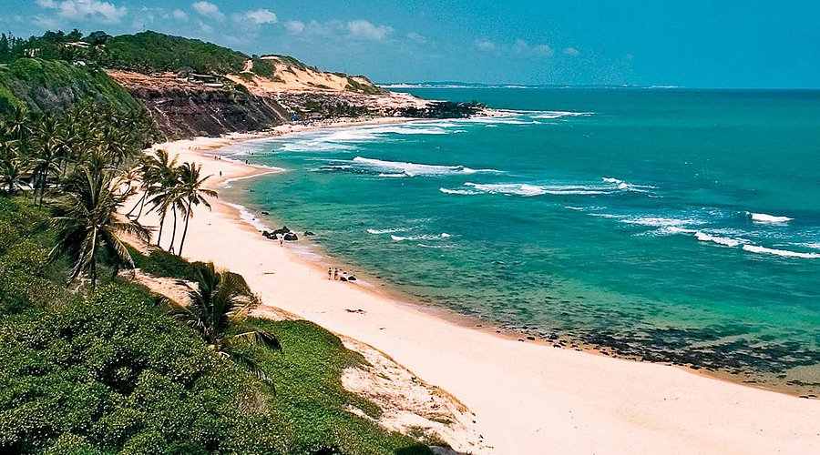 Vista aérea da Praia da Pipa, Rio Grande do Norte, com suas falésias coloridas, mar azul com ondas e coqueiros na areia, um local vibrante para casais.