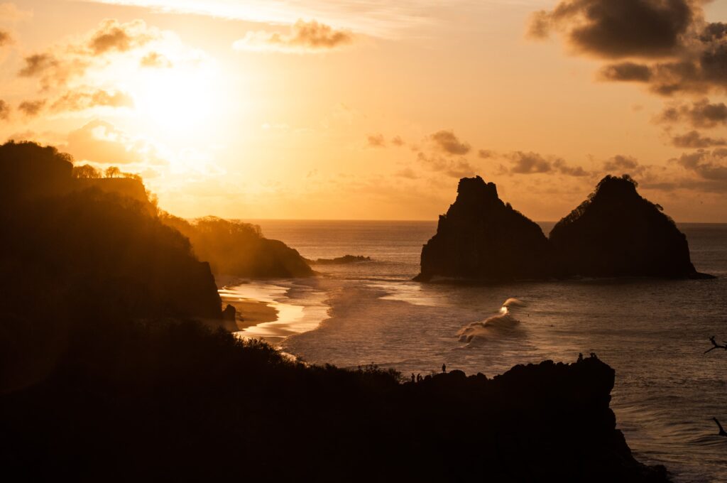 Morro Dois Irmãos em Fernando de Noronha, Pernambuco, com águas cristalinas em tons de azul e verde e formações rochosas imponentes, um destino romântico paradisíaco.