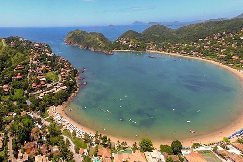 Vista aérea da Praia da Ferradura em Búzios, Rio de Janeiro, com sua enseada em formato de ferradura, barcos na água e casas na encosta, ideal para um dia de relaxamento a dois.