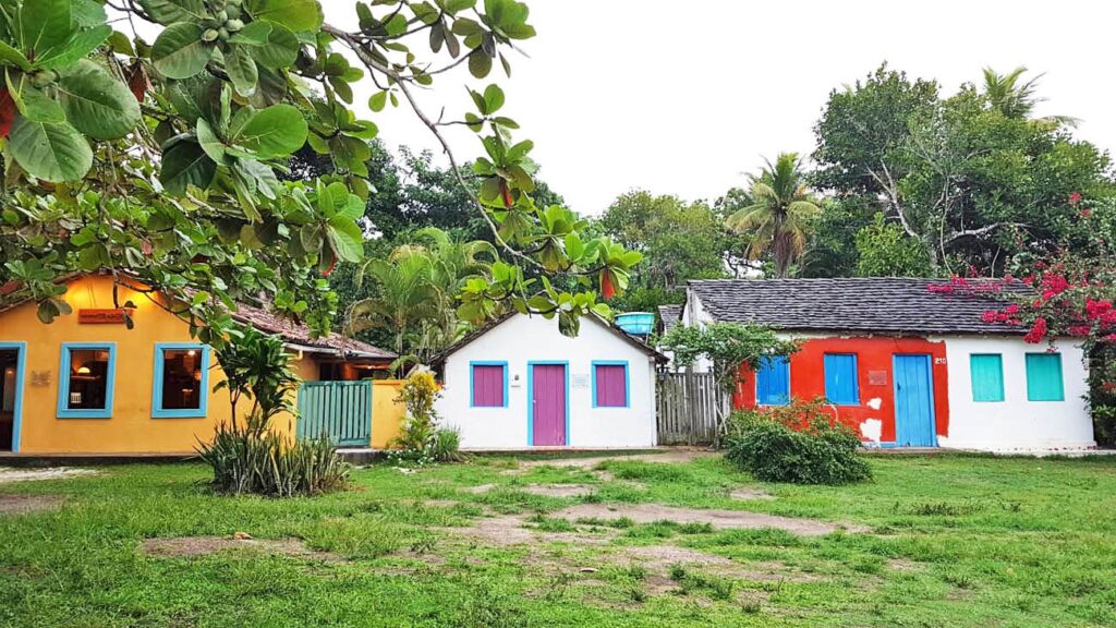 Casas coloridas e charmosas no Quadrado de Trancoso, Bahia, com arquitetura rústica e jardins verdes, um ambiente boêmio e romântico para casais.